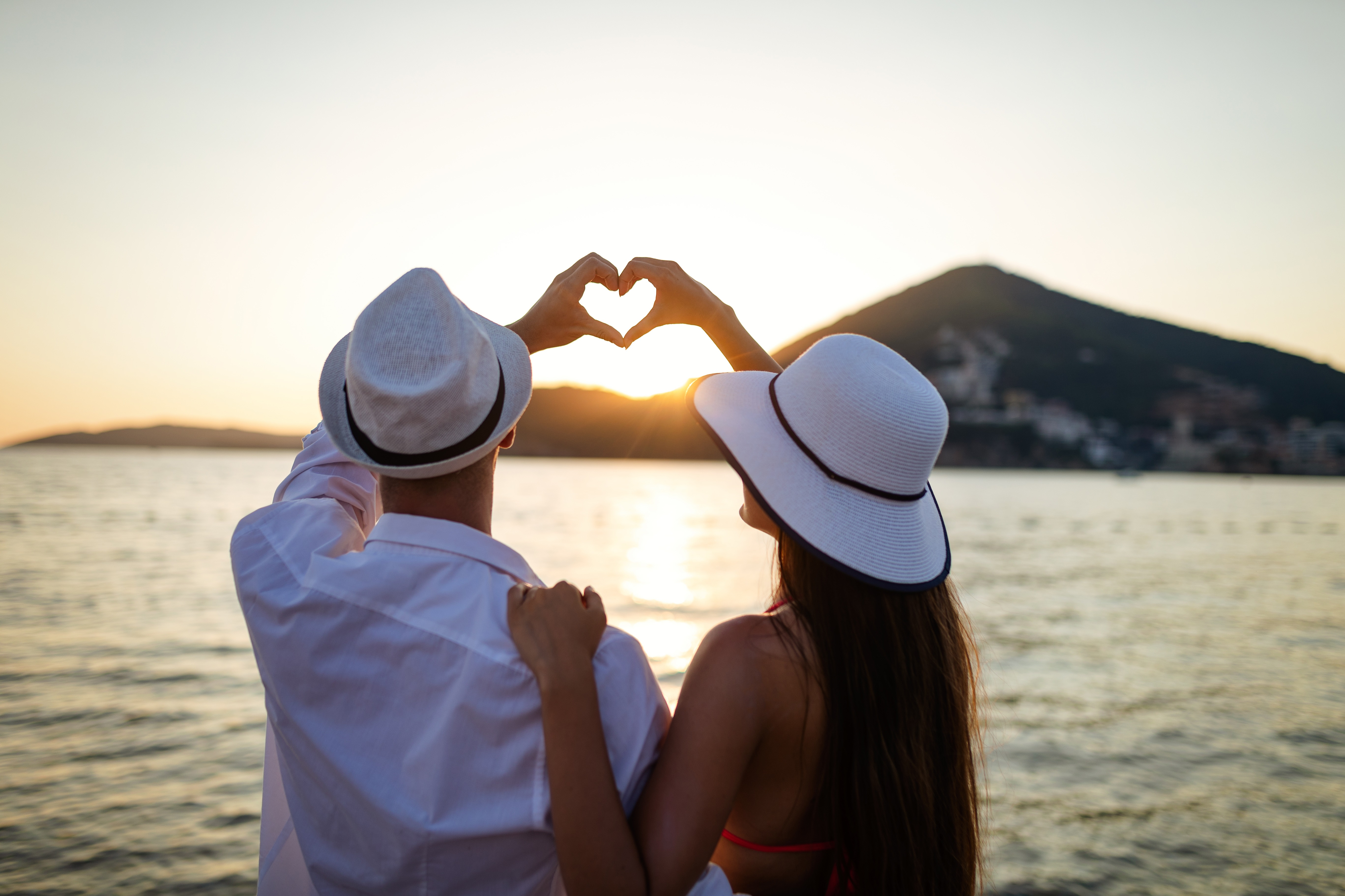 Paar am Strand bei Sonnenunterang formt zusammen mit den Händen ein Herz