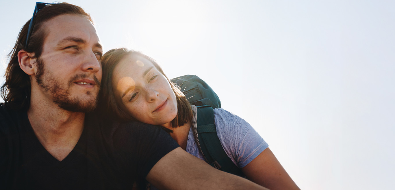 Mann und Frau die aneinander gelehnt vor einem blauem Himmel sitzen.
